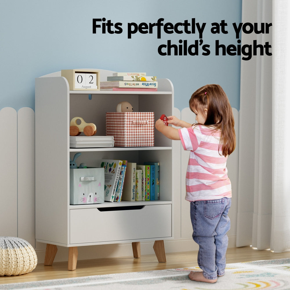 Child reaching for a toy on a white shelf with wooden legs in a room.