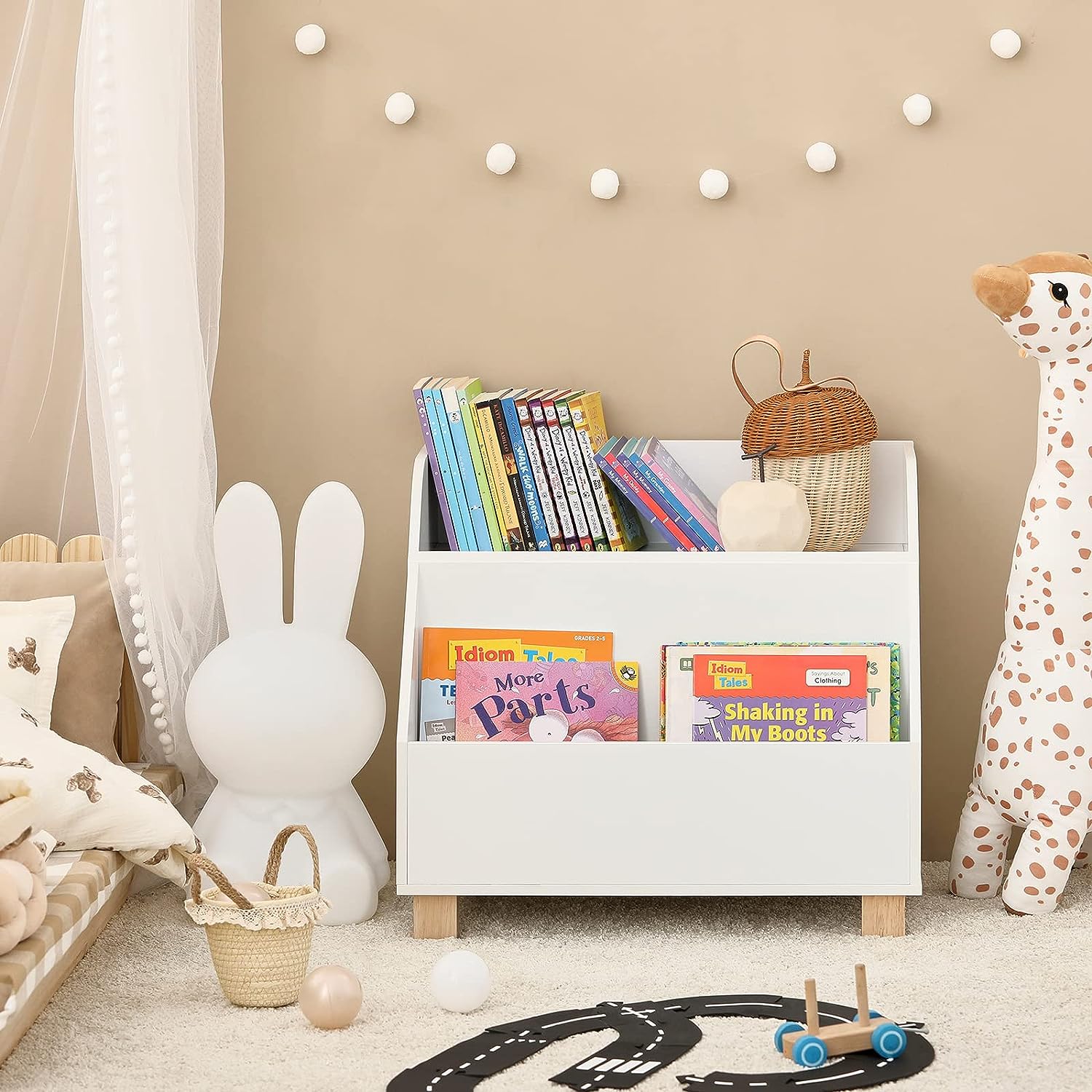 Children's room with a white bookshelf filled with books, surrounded by toys and decor.