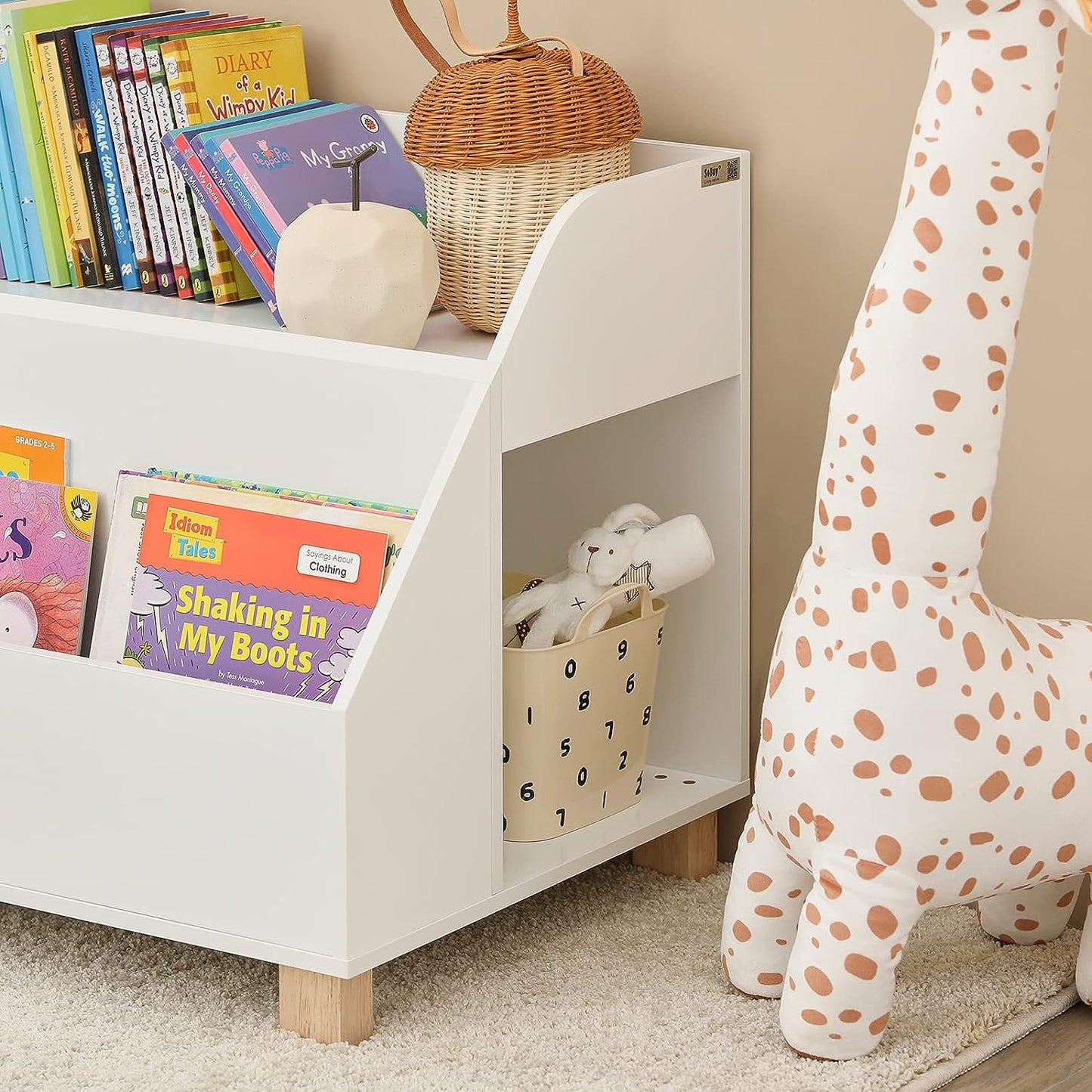 Children's bookshelf with books and toys next to a giraffe plush toy.