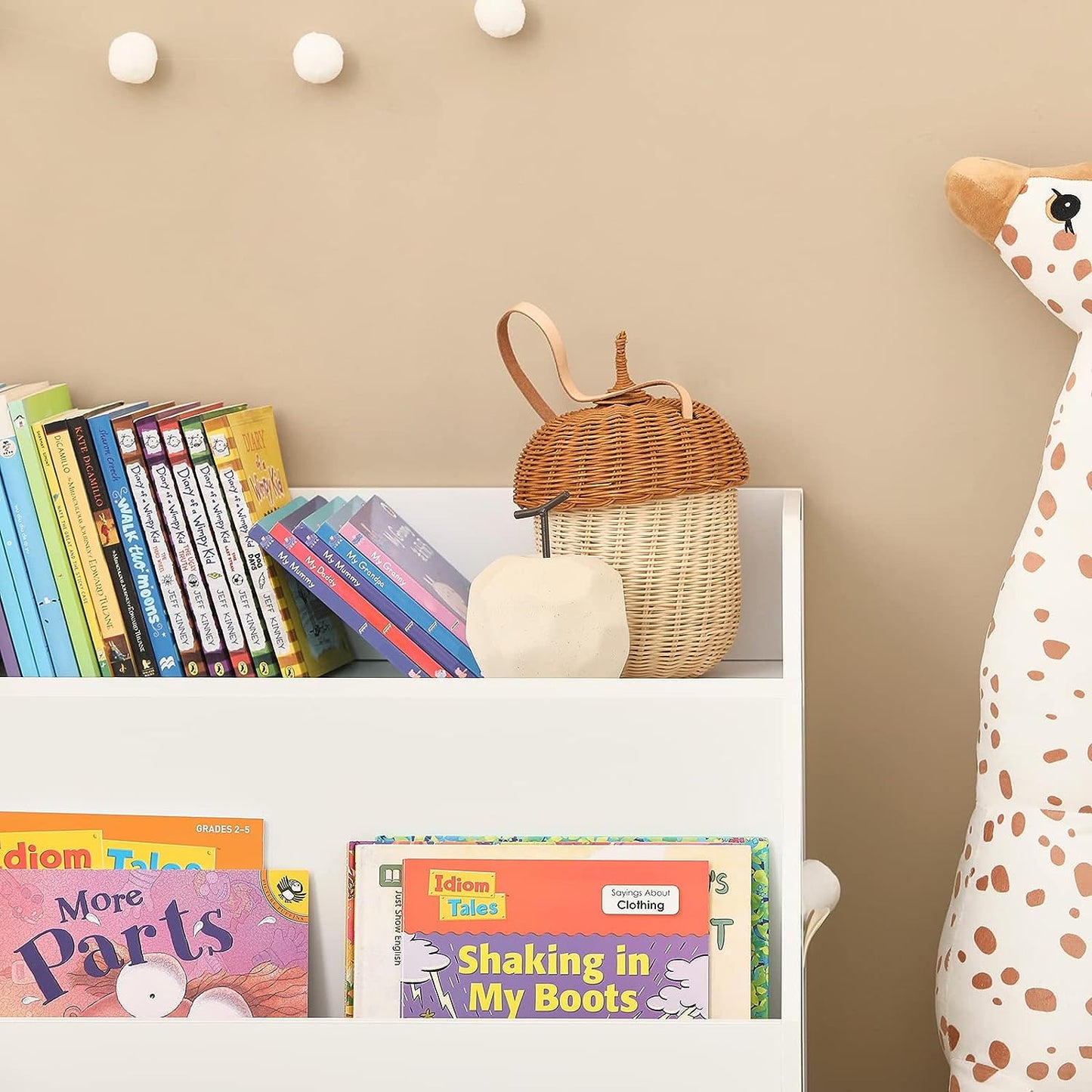 Children's books on a shelf with a wicker basket and stuffed giraffe toy against a beige wall.