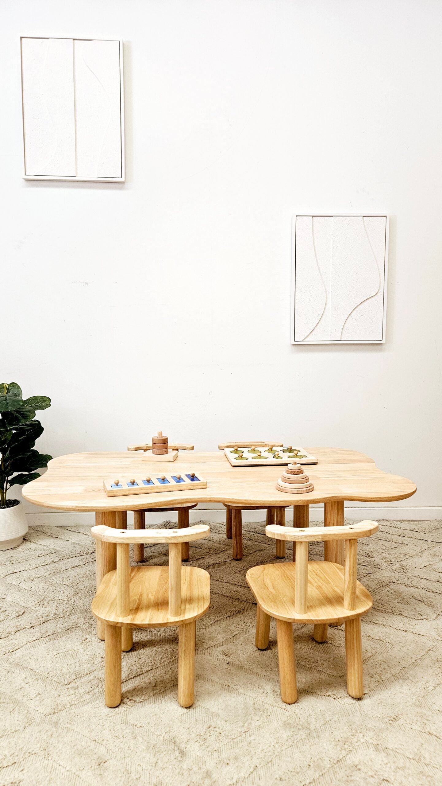 Wooden dining table with chairs in a minimalistic room with white walls and a plant.